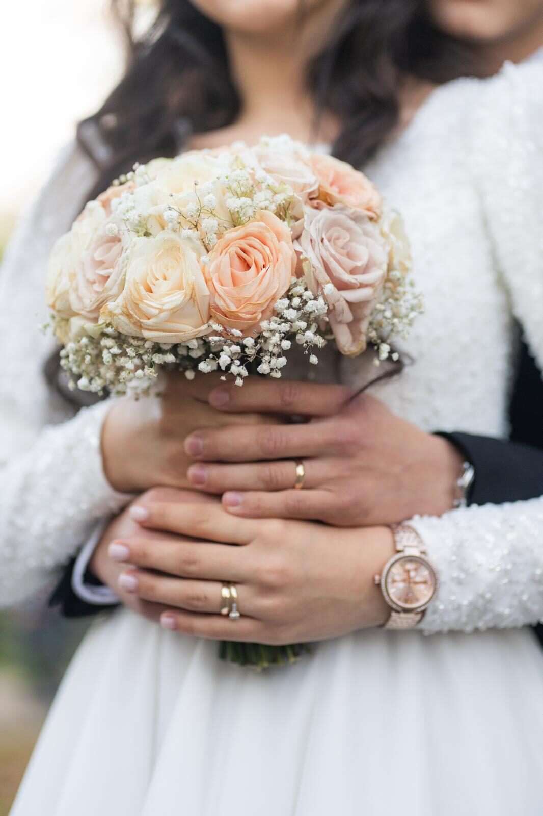 Couple holding a bridal bouquet with rings