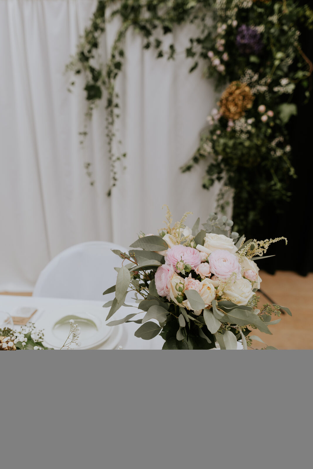 Blush wedding bouquet on a styled top table with floral arch
